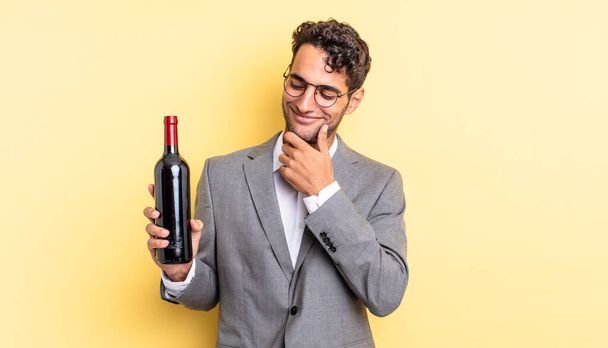 hispanic handsome man smiling with a happy, confident expression with hand on chin. wine bottle concept - Foto, imagen