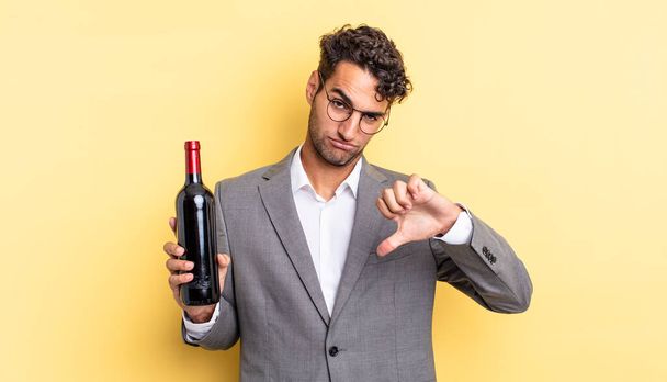 hispanic handsome man feeling cross,showing thumbs down. wine bottle concept - Foto, Imagen