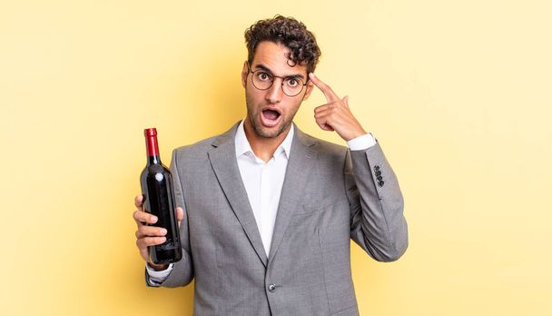 hispanic handsome man looking surprised, realizing a new thought, idea or concept. wine bottle concept - Fotografie, Obrázek