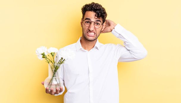 hispanic handsome man feeling stressed, anxious or scared, with hands on head. flowers pot concept - Zdjęcie, obraz