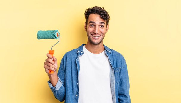 hispanic handsome man looking happy and pleasantly surprised. roller paint concept - Photo, image