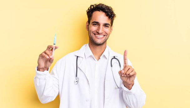 hispânico bonito homem sorrindo orgulhosamente e confiantemente fazendo número um médico e srynge conceito - Foto, Imagem