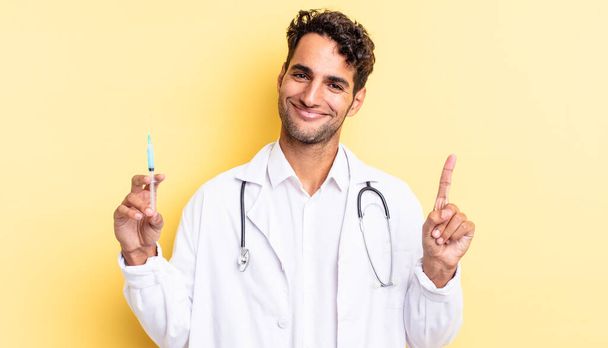 hispanic handsome man smiling and looking friendly, showing number one physician and srynge concept - Φωτογραφία, εικόνα