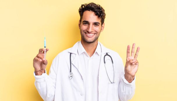 hispanic handsome man smiling and looking friendly, showing number three physician and srynge concept - Foto, Bild