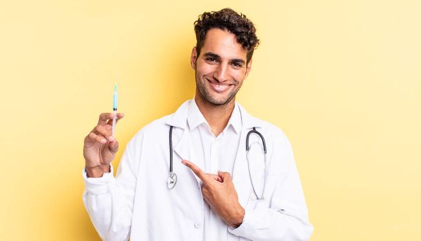 hispanic handsome man smiling cheerfully, feeling happy and pointing to the side physician and srynge concept - Photo, Image