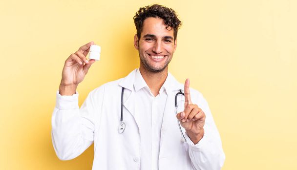 hispanic handsome man smiling proudly and confidently making number one. physician bottle pills concept - 写真・画像