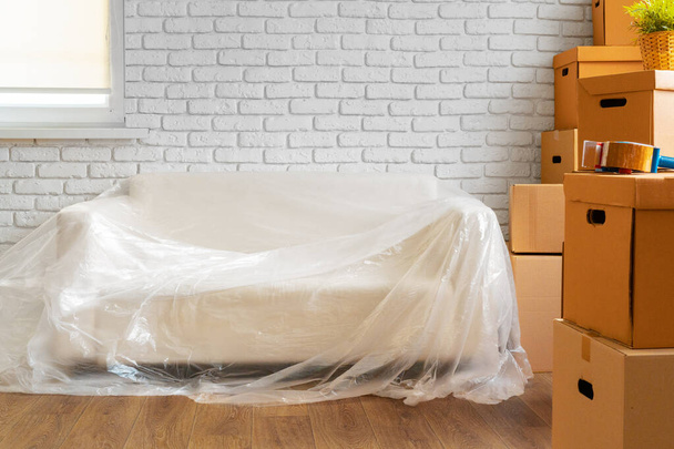 Упакованный диван и стопка картонных коробок в комнате. Концепция движения - Фото, изображение