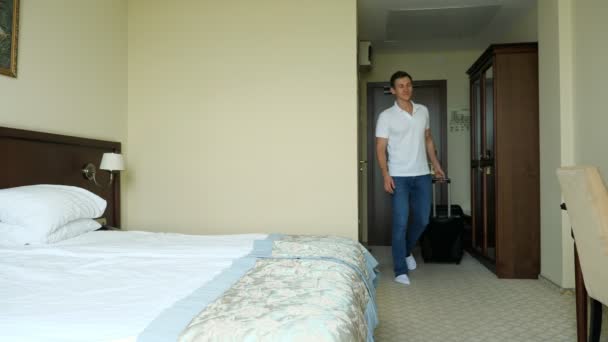 Junger Mann mit Koffer betritt Hotelzimmer und fällt zufrieden aufs Bett - Filmmaterial, Video