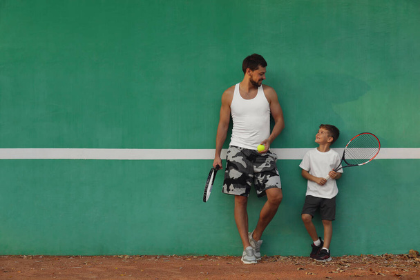 Father with his son near green wall on tennis court. Space for text - Фото, зображення