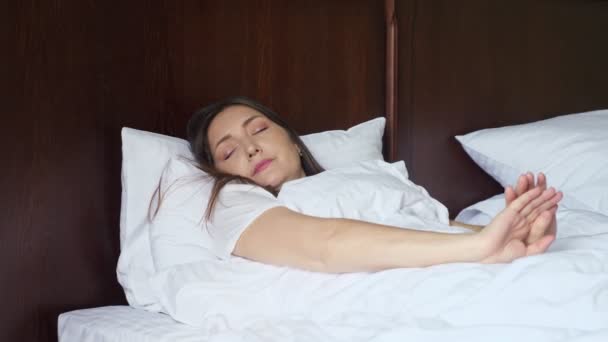 młoda kobieta budzi się i rozciąga leżąc w łóżku - Materiał filmowy, wideo