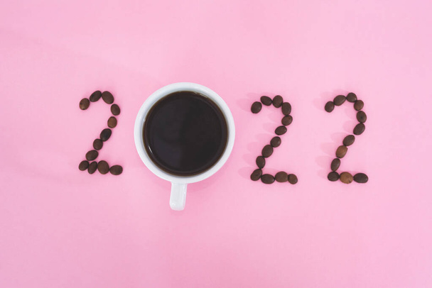 Nieuwjaar, nummers 2022 aangelegd uit koffie op roze achtergrond, kopje koffie en koffiebonen - Foto, afbeelding