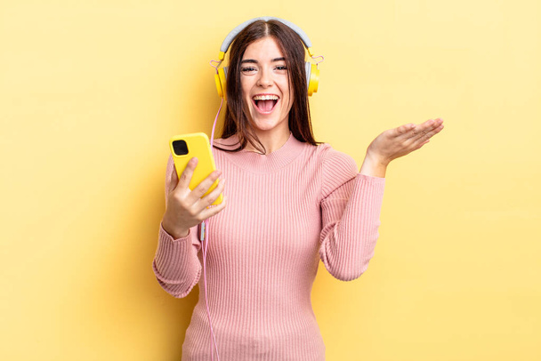 A fiatal spanyol nő boldog és csodálkozik valami hihetetlen dolgon. fejhallgató és telefonkoncepció - Fotó, kép