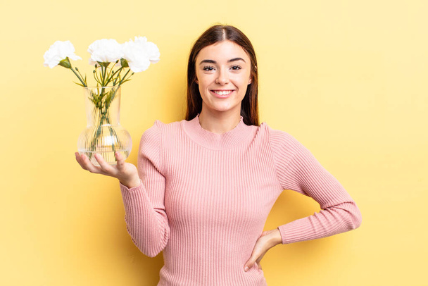 young hispanic woman smiling happily with a hand on hip and confident. flower pot concept - Foto, Imagen