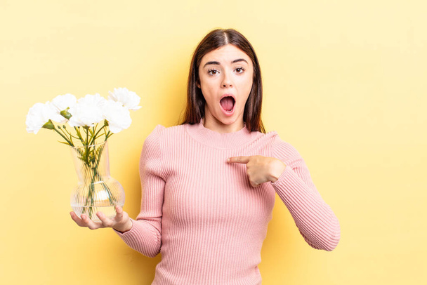 young hispanic woman looking shocked and surprised with mouth wide open, pointing to self. flower pot concept - 写真・画像