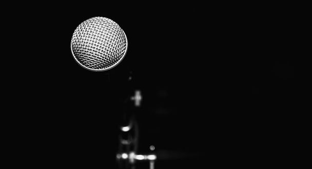 Öffentlicher Auftritt am Bühnenmikrofon vor schwarzem Hintergrund. Kopierraum. Schwarz-Weiß-Foto - Foto, Bild