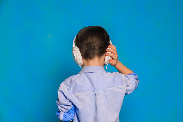 A boy with headphones on a blue background . Children's headphones. Harm of headphones for the child. Useful audiobooks for children. An article about children's leisure. Music. Copy Space - Foto, afbeelding