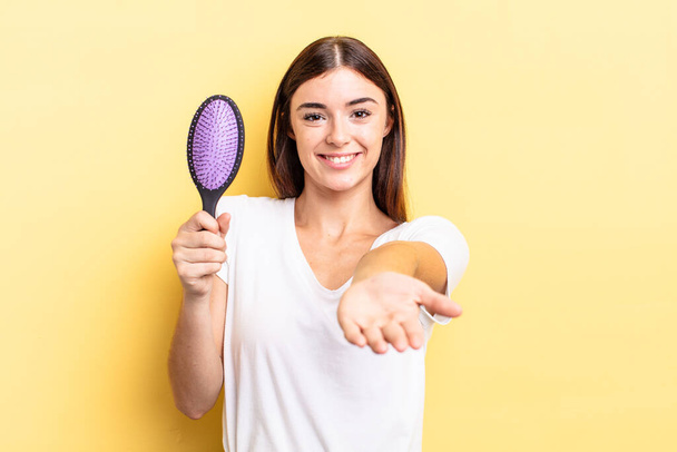 young hispanic woman smiling happily with friendly and  offering and showing a concept. hair brush concept - Фото, изображение