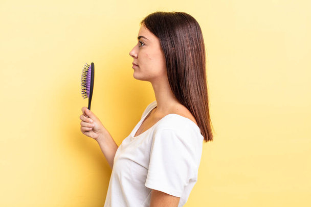 young hispanic woman on profile view thinking, imagining or daydreaming. hair brush concept - Photo, image