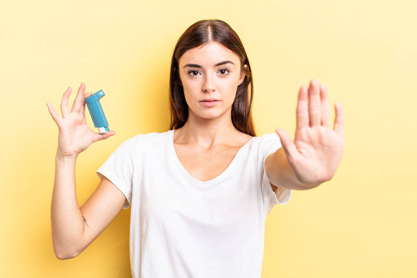 young hispanic woman looking serious showing open palm making stop gesture. asthma concept - 写真・画像