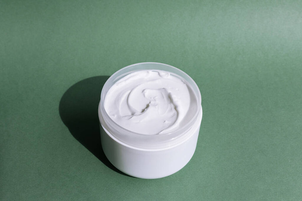 Tarro abierto blanco de crema se levanta sobre un fondo verde - Foto, imagen