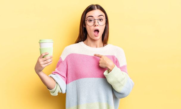 young hispanic woman looking shocked and surprised with mouth wide open, pointing to self. take away coffee concept - Foto, afbeelding