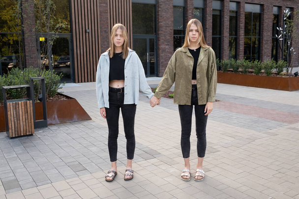 Blonde Zwillingsmädchen halten sich an der Hand, während sie gegen modernes Gebäude stehen - Foto, Bild