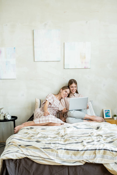 Felices gemelos adolescentes sentados en la cama y viendo películas en línea - Foto, Imagen