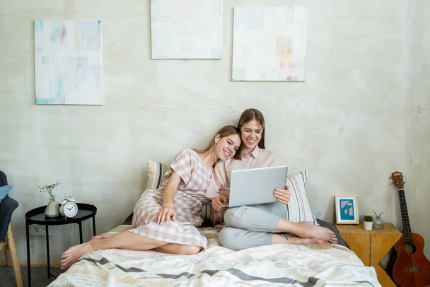 Δύο χαρούμενα και στοργικά έφηβα κορίτσια που βλέπουν online ταινία στο κρεβάτι - Φωτογραφία, εικόνα