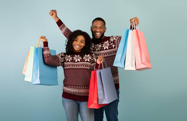 Bereit für das Neujahrsfest. Glückliches afrikanisch-amerikanisches Paar mit vielen bunten Einkaufstüten vor blauem Hintergrund - Foto, Bild