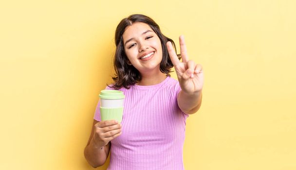 young hispanic woman smiling and looking happy, gesturing victory or peace. take away coffee concept - Foto, Imagem