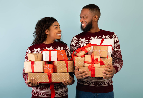 Αγαπημένοι μαύροι σύζυγοι κουβαλάνε ένα σωρό χριστουγεννιάτικα κουτιά δώρου και χαμογελούν ο ένας στον άλλο, έτοιμοι να γιορτάσουν την Πρωτοχρονιά - Φωτογραφία, εικόνα