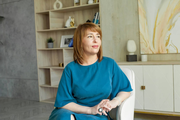 Pozitív középkorú nő ül karosszékben otthon - Fotó, kép