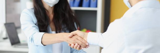 Fiatal üzletemberek orvosi maszkban kezet ráznak a munkaasztalnál. - Fotó, kép