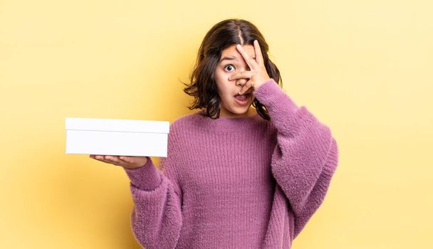 young hispanic woman looking shocked, scared or terrified, covering face with hand. blank box concept - Fotó, kép
