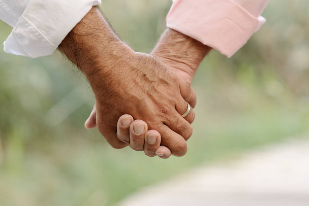 Nahaufnahme eines homosexuellen Paares, das sich zärtlich an den Händen hält, während es einen gemeinsamen Spaziergang im Freien genießt. - Foto, Bild