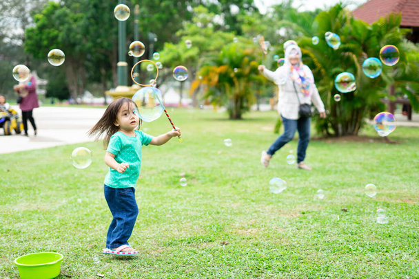 Lovely active little asian girl playing with soap bubble outdoor in the park - Foto, Imagem