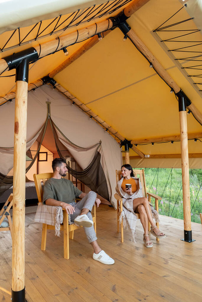 Young restful man and woman relaxing in armchairs by glamping house - Foto, imagen