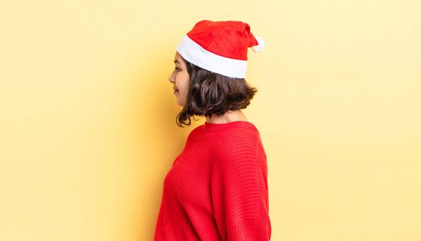 young hispanic woman on profile view thinking, imagining or daydreaming. christmas concept - 写真・画像