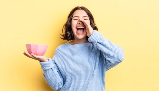 young hispanic woman feeling happy,giving a big shout out with hands next to mouth. empty bowl concept - Fotoğraf, Görsel