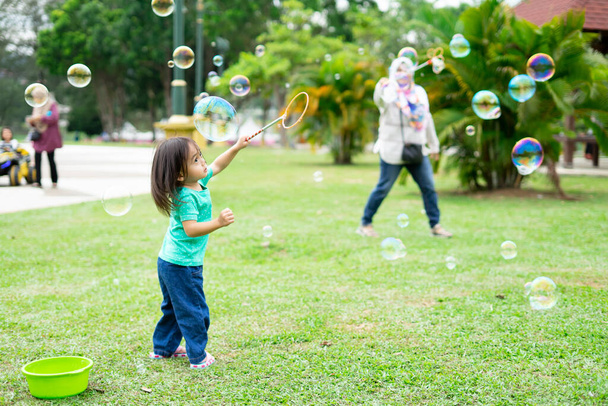 Precioso activo poco asiático chica jugando con jabón burbuja al aire libre en el parque - Foto, imagen