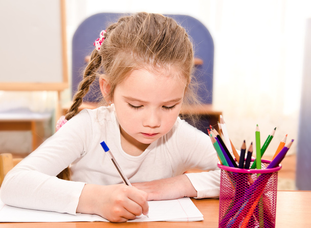 Милая маленькая девочка пишет за столом.
  - Фото, изображение