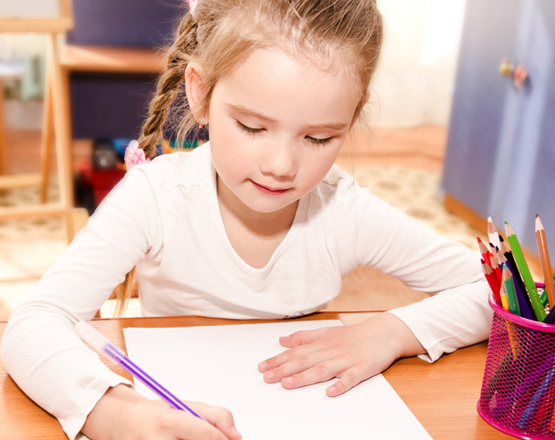 Cute little girl is writing at the desk   - Фото, зображення