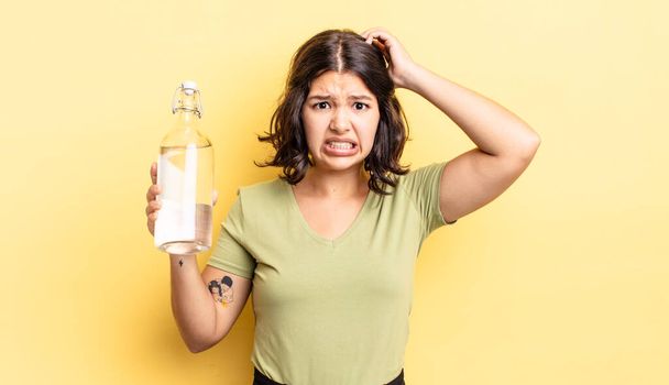 young hispanic woman feeling stressed, anxious or scared, with hands on head. water bottle concept - Foto, Imagem