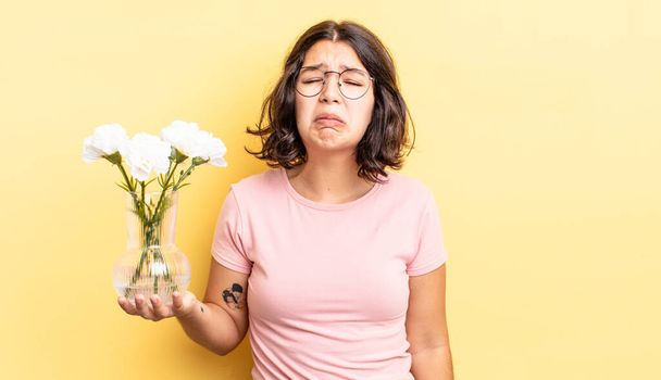 young hispanic woman feeling sad and whiney with an unhappy look and crying. flowers pot concept - Фото, изображение
