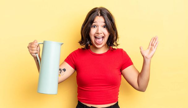 young hispanic woman feeling happy and astonished at something unbelievable. thermos concept - Photo, Image