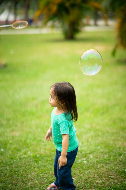Precioso activo poco asiático chica jugando con jabón burbuja al aire libre en el parque - Foto, Imagen