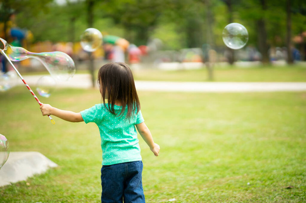 Lovely active little asian girl playing with soap bubble outdoor in the park - Photo, Image