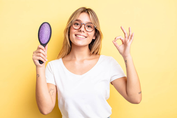 pretty blonde girl feeling happy, showing approval with okay gesture. hair brush concept - Fotoğraf, Görsel
