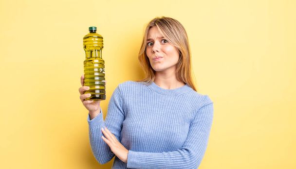 pretty blonde girl shrugging, feeling confused and uncertain. olive oil concept - Photo, image