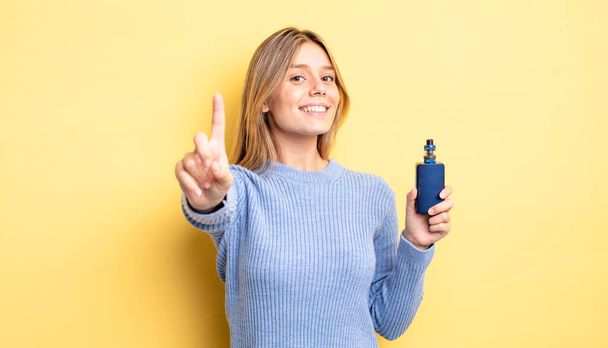 pretty blonde girl smiling proudly and confidently making number one. smoke vaporizer concept - Zdjęcie, obraz